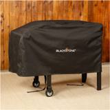 Blackstone 1529 cover on a griddle cart against a wood wall, buckle straps hanging loose by the legs