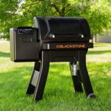 Blackstone 900 pellet grill on a lawn, hood closed, control dial on the hopper and a small pail hanging under the barrel