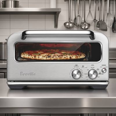 Breville Smart Oven Pizzaiolo in brushed stainless on a kitchen bench, a pizza baking inside