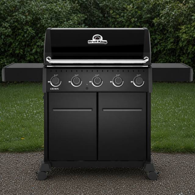 Black Broil King Crown 520 Shadow gas grill on gravel, lid closed, five knobs above two cabinet doors, hedge behind