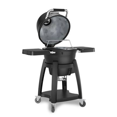 Broil King Keg Kamado Charcoal grill, black keg-shaped body on a wheeled cart, on patio flagstones at dusk