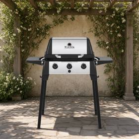 Broil King Porta-Chef 320 portable gas grill on a deck, lid closed, black cast cookbox with stainless lid insert and drop-down side shelves, seen from the front left