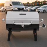 Char-Broil 465640214 portable gas grill, stainless lid latched shut, standing on its folding legs behind a van