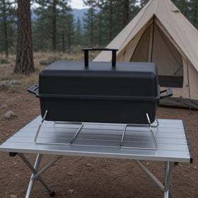 Black Char-Broil portable charcoal grill open on a camp table, pine trees and a tent behind it