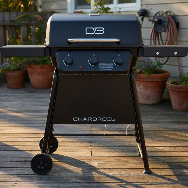 Black Char-Broil 3-burner gas grill on a weathered deck, lid closed, both side shelves out, potted plants behind