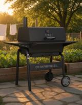 Black Char-Broil C-Line 840 charcoal grill on a garden path, lid closed, smokestack at the right and the CHARBROIL name across the front shelf