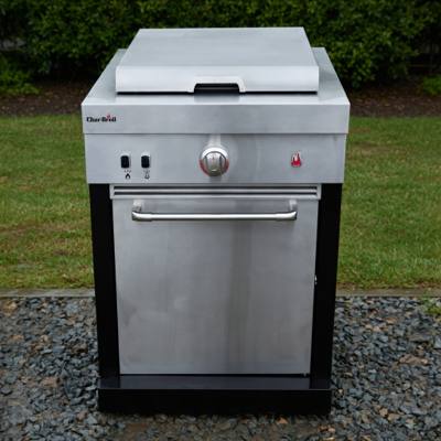 Char-Broil Medallion griddle module on gravel beside a lawn, stainless cabinet, lid closed, black corner posts
