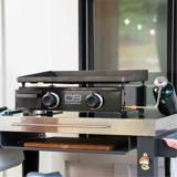Char-Broil 22-inch tabletop griddle set up on a prep cart by a doorway, green propane cylinder hooked to its side