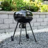 Char-Griller 22-inch black kettle grill standing on gray gravel in front of a stone garden wall, lid closed