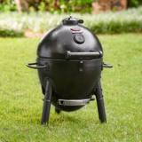 Black AKORN Jr. kamado standing on grass, lid latched, with its lower damper and ash pan under the bowl