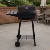 Char-Griller Patio Pro barrel charcoal grill with its slatted side shelf, on a patio with a brick wall