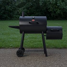 Black Char-Griller Smokin' Pro barrel smoker on wet gravel, side fire box at right, smokestack up, hedge behind