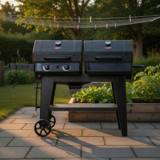 Char-Griller Texas Trio on flagstones at golden hour, twin black lids closed, a gauge on each, side shelf and cart wheels