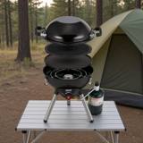 Coleman 4-in-1 cooking system stacked on a camp table, wok, grill plate and burner visible, propane cylinder alongside and a tent behind
