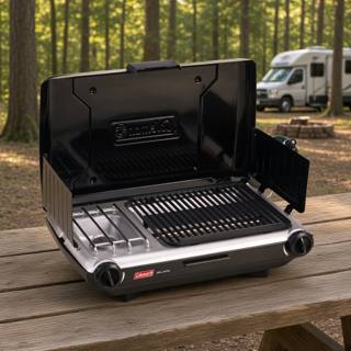 Coleman 2209294 tabletop grill and stove open on a picnic table at a wooded campsite, grate beside the burner