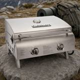 Cuisinart CGG-306P stainless tabletop gas grill, lid closed, standing on a rock outdoors with a backpack behind it