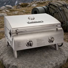Cuisinart CGG-306P stainless tabletop gas grill, lid closed, standing on a rock outdoors with a backpack behind it