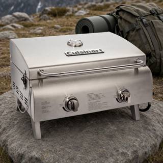 Cuisinart CGG-306P stainless tabletop gas grill, lid closed, standing on a rock outdoors with a backpack behind it