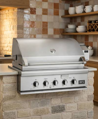 DCS 36-inch stainless steel built-in gas grill set into a stone outdoor kitchen counter, hood closed