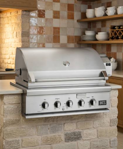 DCS 36-inch stainless steel built-in gas grill set into a stone outdoor kitchen counter, hood closed