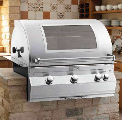 Fire Magic Aurora A660i set into a stone island, hood closed, viewing window and four control knobs visible