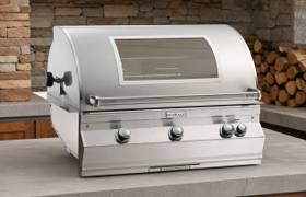 Fire Magic Aurora A790i in a concrete counter inside a brick alcove, hood closed, window and four knobs visible
