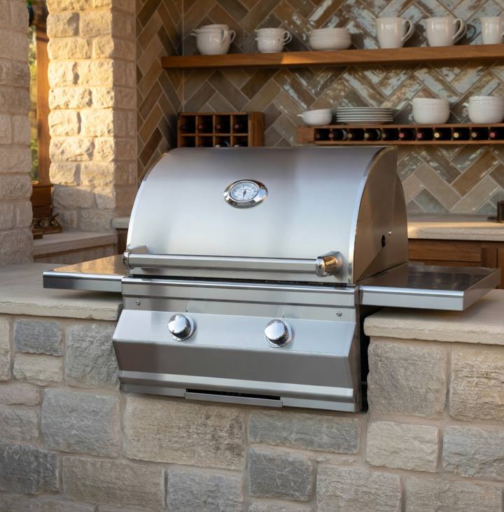 Fire Magic C430i stainless head built into a pale stone counter, lid down, hood gauge above two knobs