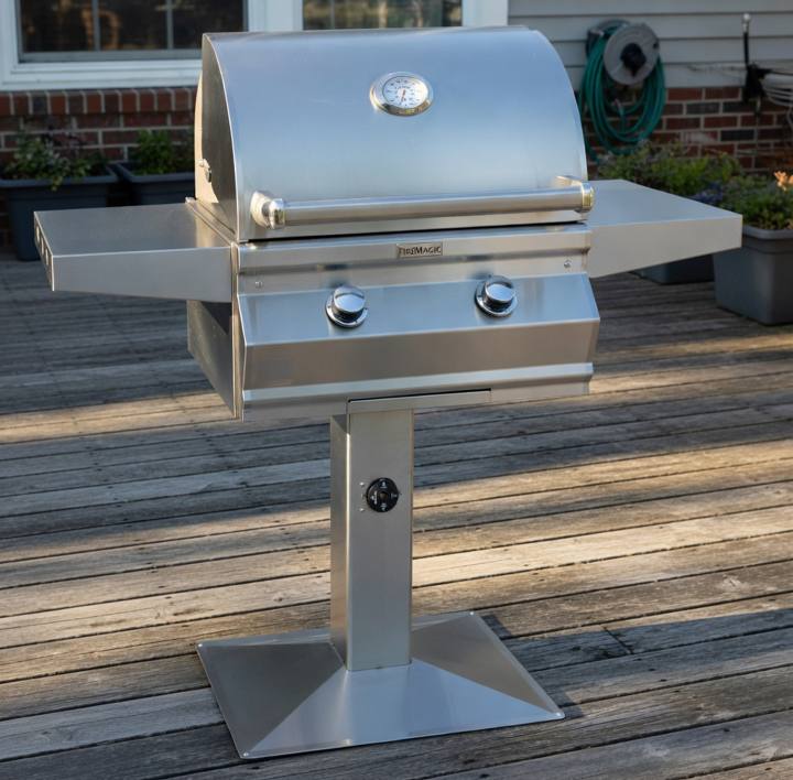 Fire Magic CM430s stainless grill on a post with a square base plate, bolted to a gray timber deck, timer dial on the post