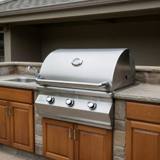 Fire Magic CM540 stainless grill head set into a stone outdoor counter, hood closed, three knobs and a lid dial