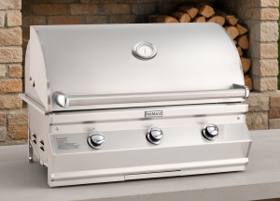 Fire Magic CM650i stainless grill head, hood closed with lid thermometer and three knobs, on stone before stacked firewood