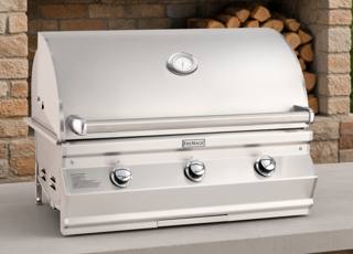 Fire Magic CM650i stainless grill head, hood closed with lid thermometer and three knobs, on stone before stacked firewood