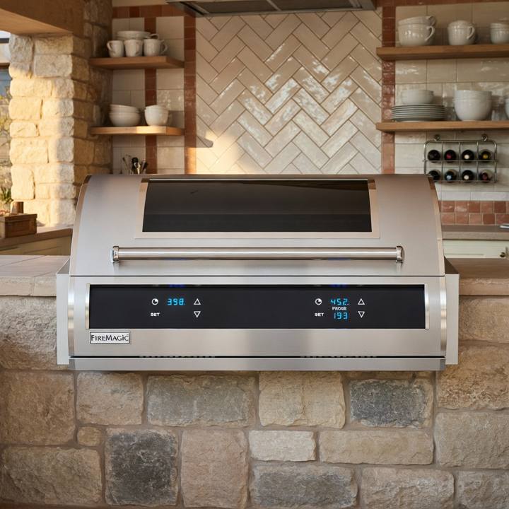 Fire Magic EL500i built into a stone counter, hood closed with a dark glass window and two lit touch control displays
