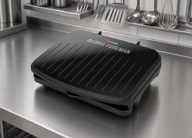 George Foreman Classic Plate grill closed on a stainless prep bench, ribbed black lid, red and green lights
