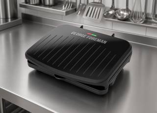 George Foreman Classic Plate grill closed on a stainless prep bench, ribbed black lid, red and green lights