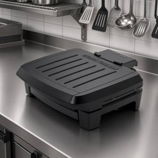 George Foreman Submersible contact grill closed on a stainless prep bench, black ribbed lid, control probe at the rear
