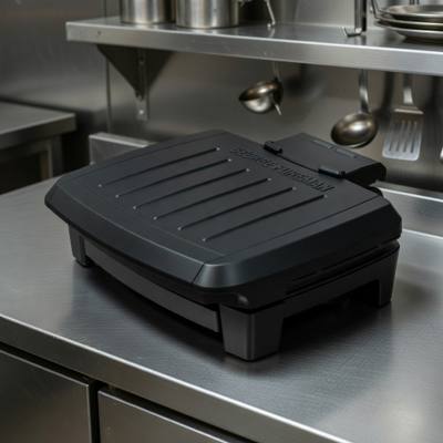 George Foreman Submersible contact grill closed on a stainless prep bench, black ribbed lid, control probe at the rear
