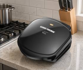 George Foreman GR10B closed on a marble worktop beside a gas hob, amber lamp lit on its lid