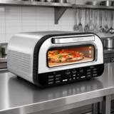 Gourmia stainless indoor pizza oven on a steel kitchen counter, a pizza behind the window