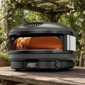 Gozney Arc gas pizza oven on a wooden table under a pergola, flame lit and dial showing 950