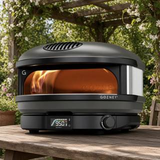 Gozney Arc gas pizza oven on a wooden table under a pergola, flame lit and dial showing 950