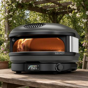 Gozney Arc gas pizza oven on a wooden table under a pergola, flame lit and dial showing 950
