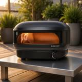 Gozney Arc Lite on a steel outdoor table on a timber deck, flame lit inside