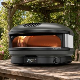 Gozney Arc XL on a wooden table under a pergola, flame lit and display reading 450