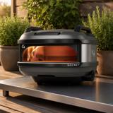Gozney Tread with its carry handles on a steel outdoor table on a timber deck, flame lit inside
