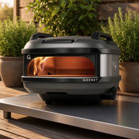 Gozney Tread with its carry handles on a steel outdoor table on a timber deck, flame lit inside