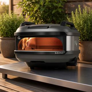 Gozney Tread with its carry handles on a steel outdoor table on a timber deck, flame lit inside