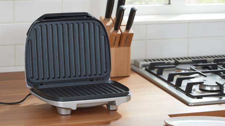 Hamilton Beach 25371 indoor grill open on a wooden kitchen counter, ribbed nonstick plates facing the camera