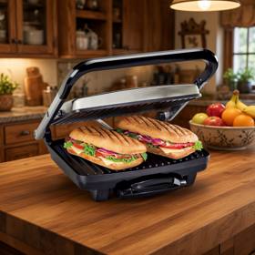 Hamilton Beach 25410MN panini press with its stainless lid raised, two pressed paninis on the ribbed lower plate