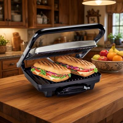 Hamilton Beach 25410MN panini press with its stainless lid raised, two pressed paninis on the ribbed lower plate