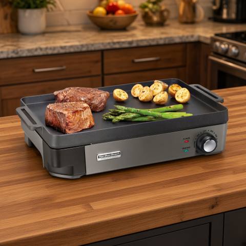 Hamilton Beach 38560 on a kitchen island, steak, potatoes and asparagus cooking on the flat cast iron plate